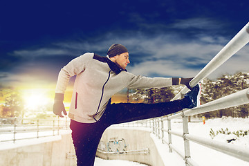 Image showing sports man stretching leg at fence in winter