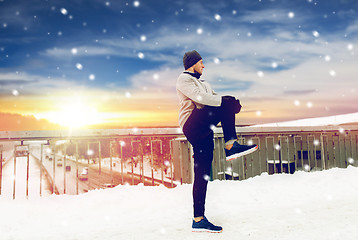 Image showing man exercising and stretching leg on winter bridge