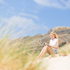 Image showing Woman reading book, enjoying sun on beach.