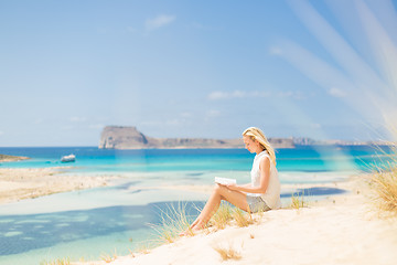 Image showing Woman reading book, enjoying sun on beach.