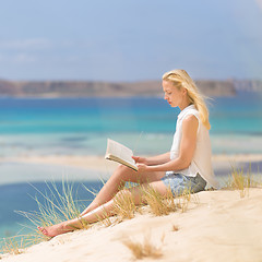 Image showing Woman reading book, enjoying sun on beach.