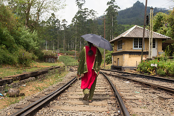 Image showing Woman wearing traditional sari and black umbrella walking on railway tracks in Sri Lanka.