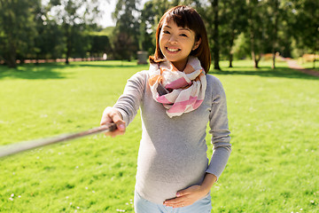 Image showing happy pregnant asian woman taking selfie at park