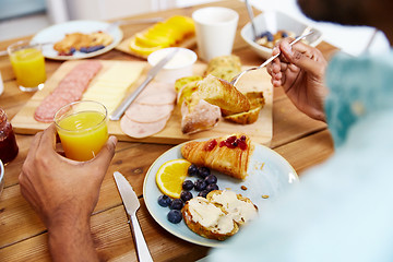 Image showing close up of man eating croissant with orange juice