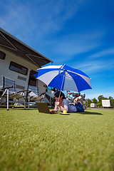 Image showing Woman on the grass, looking at the laptop under umbrella near th