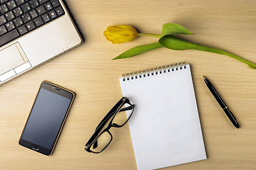 Image showing Workspace on the table are tulip, notebook, laptop, glasses, smartphone and pen