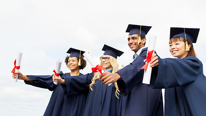 Image showing happy students in mortar boards with diplomas