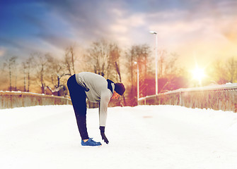 Image showing man exercising and stretching leg on winter bridge