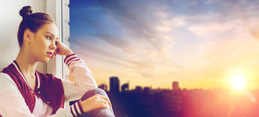 Image showing sad pretty teenage girl sitting on windowsill