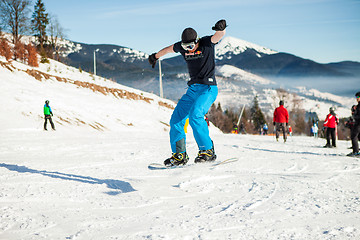 Image showing Bukovel, Ukraine - December 22, 2016: Man boarder jumping on his snowboard against the backdrop of mountains, hills and forests in the distance. Bukovel, Carpathian mountains