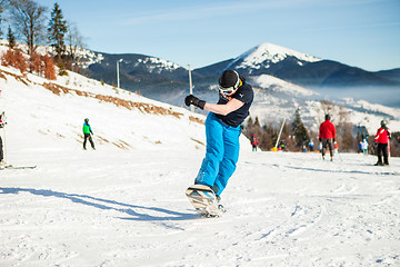 Image showing Bukovel, Ukraine - December 22, 2016: Man boarder jumping on his snowboard against the backdrop of mountains, hills and forests in the distance. Bukovel, Carpathian mountains