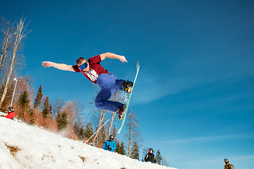 Image showing Bukovel, Ukraine - December 22, 2016: Man boarder jumping on his snowboard against the backdrop of mountains, hills and forests in the distance. Bukovel, Carpathian mountains