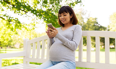 Image showing happy pregnant asian woman with smartphone at park