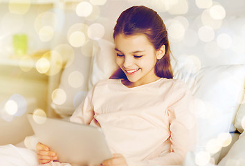 Image showing happy girl in bed with tablet pc over lights