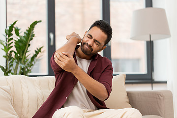 Image showing unhappy man suffering from pain in hand at home