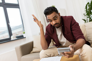 Image showing confused man with papers and calculator at home