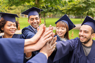 Image showing happy students in mortar boards making high five