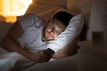 Image showing happy young man with smartphone in bed at night