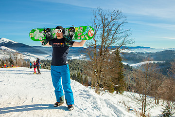 Image showing Bukovel, Ukraine - December 22, 2016: Man holding his snowboard against the backdrop of mountains, hills and forests in the distance. Bukovel, Carpathian mountains