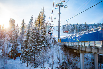 Image showing Skiers on the ski lift riding up at ski resort with beautiful background of snow-covered slopes, forests, hills in Bukovel, Ukraine