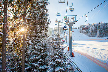 Image showing Skiers on the ski lift riding up at ski resort with beautiful background of snow-covered slopes, forests, hills in Bukovel, Ukraine