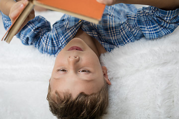 Image showing little boy is lying on the bed and reading a book