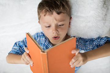 Image showing little boy is lying on the bed and reading a book