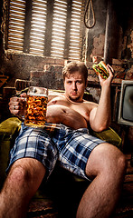 Image showing Fat man eating a hamburger sitting on a chair in the slums