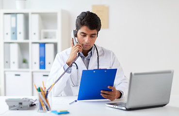 Image showing doctor with clipboard calling on phone at clinic