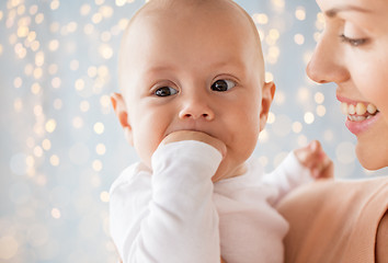 Image showing happy mother with baby sucking fingers over lights