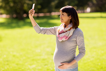 Image showing happy pregnant asian woman taking selfie at park