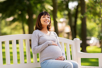 Image showing happy pregnant asian woman sitting on park bench