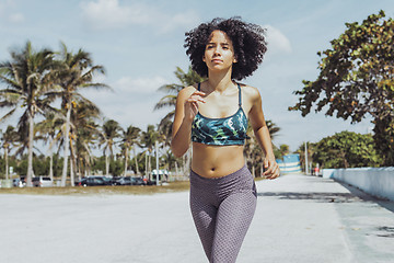 Image showing Black fit girl jogging on tropical waterfront