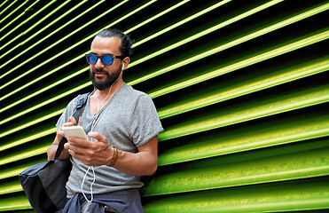 Image showing man with earphones and smartphone over wall