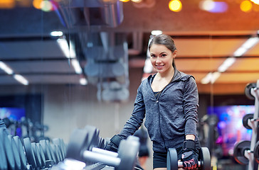 Image showing smiling young woman choosing dumbbells in gym