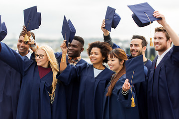 Image showing happy graduates or students waving mortar boards