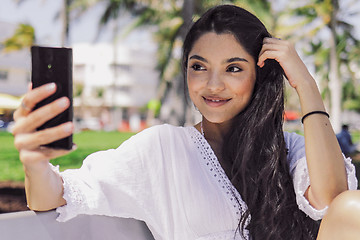 Image showing Stylish girl taking selfie on bench in park