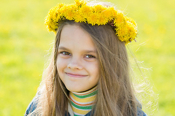 Image showing Portrait of a happy eight-year-old girl with a wreath of dandelions on her head, against the background of a spring clearing