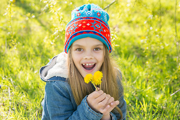 Image showing Seven-year-old girl in the spring is pleased with the blossoming dandelions