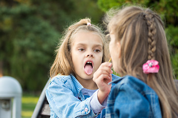 Image showing One girl treats another girl with her lollipop