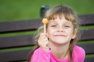 Image showing Portrait of a six-year-old cheerful girl who holds a lollipop in her hand and looks pleased at the frame