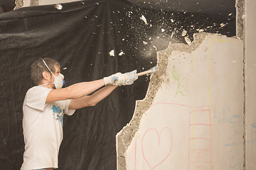 Image showing A young man breaks a partition in the apartment with a hammer