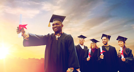 Image showing happy students in mortar boards with diplomas