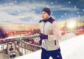 Image showing man in earphones running along winter bridge