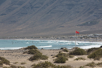 Image showing The red flag weighs in the wind at Surfers Beach Famara on Lanza