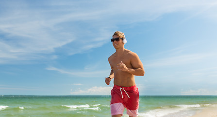 Image showing happy man with headphones running along beach