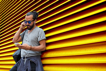 Image showing man with earphones and smartphone over wall