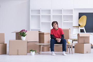 Image showing boy sitting on the table with cardboard boxes around him