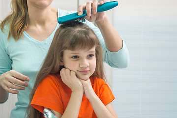 Image showing A beautiful daughter looks cute in the mirror while Mom combs her hair