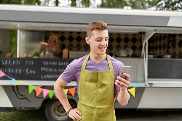 Image showing salesman in apron with smartphone at food truck